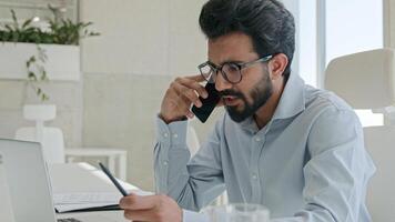 Busy Arabian Indian muslim man successful entrepreneur employer CEO boss leader executive manager businessman talking mobile phone in office workplace using laptop consult client business discussion photo