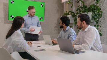 Office conference meeting with green chroma key screen male CEO leader talk to diverse multiracial businessmen and businesswoman explain colleagues paper data analysis business plan marketing strategy photo