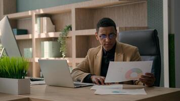 African American man entrepreneur office manager guy male businessman working at desk with laptop read documents check graphics charts business paperwork analyzing data upset financial problem mistake photo