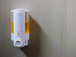 The white liquid soap container with yellow liquid inside is attached to the ceramic wall. Concept of hygiene photo