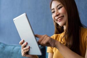 Portrait of Young attractive asian woman resting on sofa and using and looking at tablet pc in modern room communication and lifestyle concept. reading digital gadget at house. photo