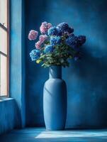 A blue vase holds vibrant hydrangeas against a matching blue background, creating a serene ambiance. photo