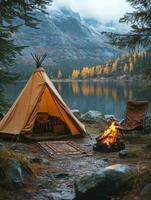 A cozy campsite by a lake with a tent, fire, and scenic mountains in the background. photo