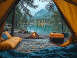 Cozy camping scene with a tent, fire, and serene lake view surrounded by mountains. photo