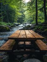 A wooden picnic table by a serene stream surrounded by lush greenery. photo