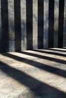 Black steel beams intersect dramatically, casting bold shadows across a smooth concrete surface, creating a modern and sleek architectural background with ample space for text overlay photo