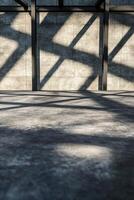 In a striking architectural setting, overlapping black steel beams create linear patterns of shadows across a smooth concrete surface, offering a sleek and dramatic aesthetic photo