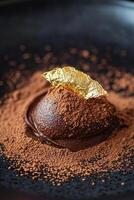 Indulge in a rich dark chocolate mousse, elegantly adorned with cocoa powder and a shimmering gold leaf, displayed on a sleek matte black plate photo