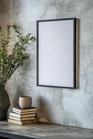 A sleek picture frame with a thin black border is mounted on a textured concrete wall. It is accompanied by a ceramic vase and a stack of books, enhancing the minimalist decor photo