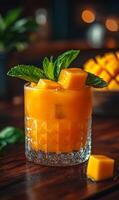 Minty mango cocktail refreshment. A vibrant mango cocktail is presented in a glass, garnished with fresh mint and mango cubes, inviting enjoyment. photo