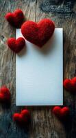 Red hearts around a blank card. Red felt hearts are scattered around a blank, textured card on a rustic wooden surface creating a romantic setting. photo