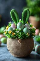 A basket of Easter eggs with green grass and bunny ears. The basket is on a table. The eggs are in different colors and sizes photo