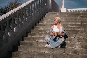 A woman sits on a set of stairs, holding a cup of coffee. She is enjoying her coffee and taking in the view from the top of the stairs. photo