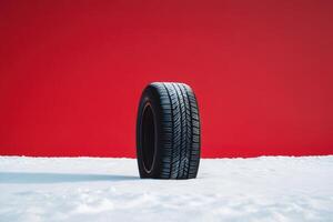 Winter tire standing on snow with vibrant red background under bright lighting photo