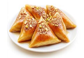 Delicious triangular pastries coated in syrup and topped with crushed nuts on a white plate photo