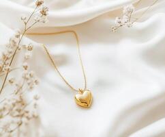 Heart-shaped gold necklace resting on soft satin fabric surrounded by delicate flowers photo