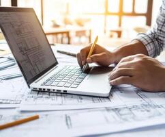 Person engaged in architectural design using laptop and sketches in bright workspace during daytime hours photo