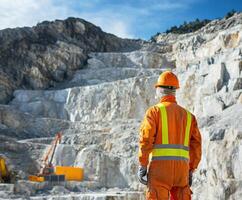 Construction worker surveys quarry site during daylight with heavy machinery in the background photo