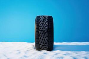 Winter tire placed on snow against a bright blue background showcasing tread design and winter conditions photo