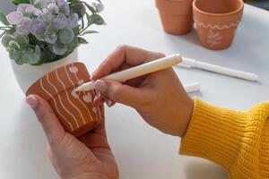 A womans hand decorates terracotta pots with white patterns using a white marker. photo