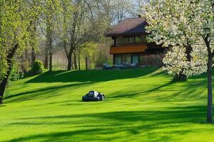Springtime garden with robotic lawn mower in lush green yard near cozy house photo