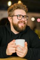 Bearded curly man smiling confident drinking coffee in restaurant or coffee shop. Millennial generation and Gen Y photo