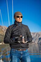 Man holding thermo mug on bow of the yacht during sailing in the morning in winter time in Adriatic sea, relaxation in yachting time. High quality photo