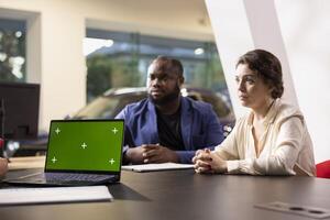 Salesman showing car features on green screen laptop to customers, hoping to close deal. Showroom agent trying to persuade clients to make purchase by presenting vehicle addons on mockup notebook photo