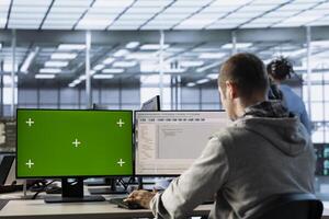 Software developer using isolated screen PC to do programming in server room providing computing resources for workloads. IT expert supervising data center supercomputers using mockup computer photo