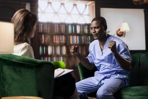 Nurse sits in serious counseling session coping with patients loss and mental health challenges. African american medical assistant working in a hospital with PTSD and trauma, powerless. photo