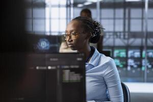 Technician in server farm ensuring compliance with industry standards and regulatory requirements. African american data center employee conducting security audits to protect against cyberthreats photo