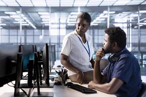 Supervisor checking on data center employee creating technical documentation for software applications. Manager supervising IT expert working in server room maintaining databases photo