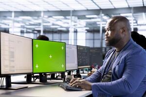 Software developer in data center using diagnostic tools on green screen PC to identify root cause of errors. IT expert working in server room on chroma key PC, repairing equipment photo
