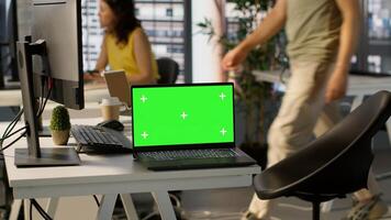 Green screen laptop on desk in workspace with admins in background doing software quality assurance. Chroma key notebook in office with woman at work inspecting coding on device, camera A photo