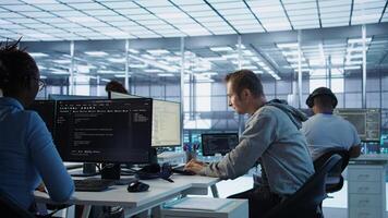 Fatigued admin stretching at work in server room to relieve muscle cramps while analyzing data on monitor. Tired man in data center relaxing body after overworking, camera B photo