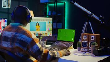 Male graphic artist using essential digital tools next to isolated mockup screen, professional design work showcasing modern setup at home. Designer showing advanced photo editing skills. Camera B.