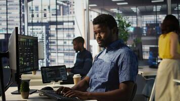 Man checking paperwork details on computer screen, solving tasks. African american bookkeeper in office making sure documents are compliant with quality assurance expectations and standards, camera B photo