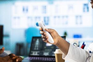 Medic measuring the temperature during checkup appointment at doctor office, using a digital thermometer tool to check for flu symptoms. Advanced healthcare services. Close up. photo