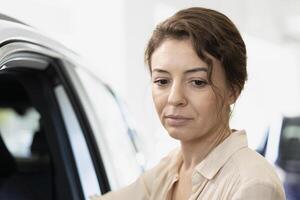 Customer in car dealership checking automobile features, comparing available models. Close up of woman checking vehicle door durability, looking to make informed purchase decision photo