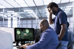 Upset coworkers in data center getting access denied notification on PC screen, trying to access server files after they were locked by hacker using ransomware, doing face palm gesture photo