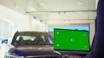 Salesperson using isolated screen laptop to present car addons options to clients, persuading them to buy. Showroom agent offers extended warranty to customers, holding chroma key notebook, camera B photo