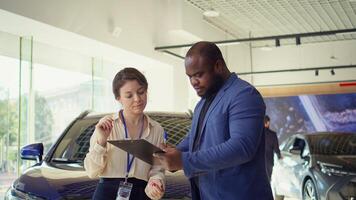 Saleswoman in car dealership signing contract with man after addressing concerns and providing compelling reasons for purchase. Agent completing necessary sale paperwork, shaking hands, camera B photo