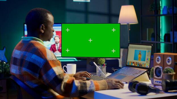 Black expert photo editor working remotely in a creative industry, using skills and software tools on dual monitors to edit images with precision. Working on freelance retouching project. Camera A.