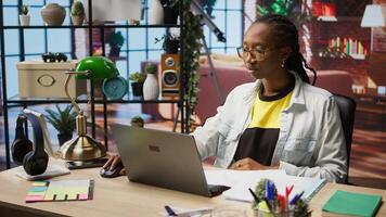 Teleworker using laptop in home office to crosscheck paper documents with online company files. Remote worker typing on notebook, inputting paperwork documentation data, camera A photo