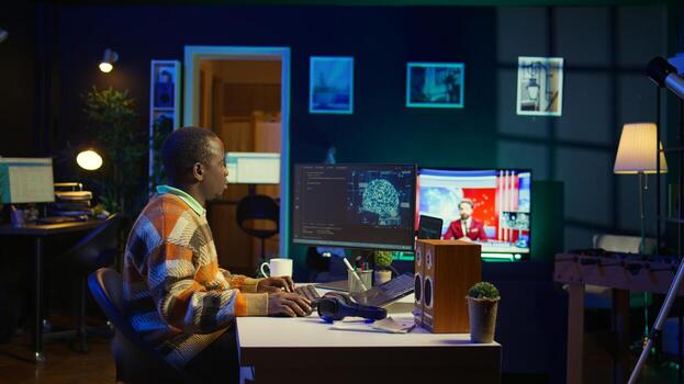 Professional male developer manages neural network at desk, working with AI code on laptop. African american IT expert freelancer developing cyber security, creating secure database. Camera B. photo