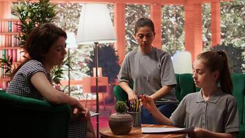 Teenage girl engages in a drawing activity as part of creative therapy session. Counseling with her mother and therapist focuses on using artwork for stress relief and emotional management. Camera B. photo