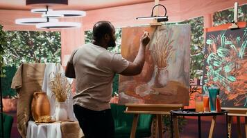 In an art studio, artist mixes a variety of watercolor paints on a palette to create a rustic masterpiece on canvas. Man painting with tools and showing his skill, artwork creation. Camera B. photo