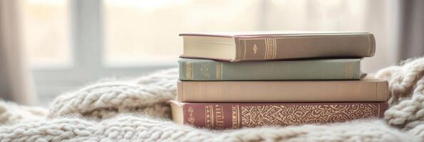 Stack of vintage books on soft blanket by window reflecting cozy reading concept photo