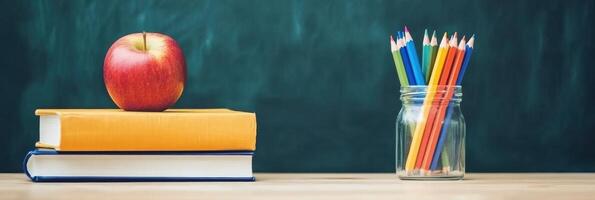 Apple on books and colored pencils in jar against chalkboard background photo
