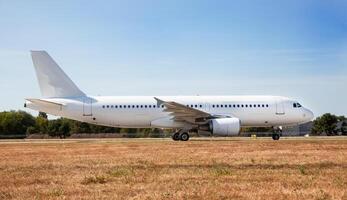 A white plane on the airport runway is taxiing. Takeoff and landing. Arrival and departure. Place for text. Passenger plane mockup. Airplane flight. Travel by air transport. Copy space photo